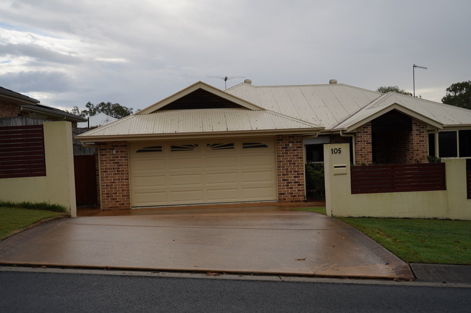 Tan coated concrete driveway and front path at a single-storey brick home with a cream garage door in Gumdale, Brisbane
