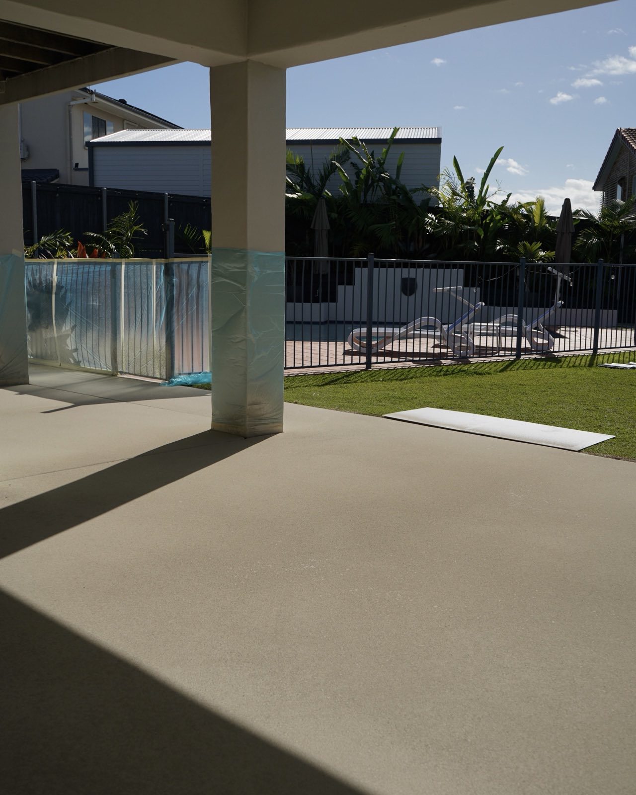 Freshly coated sand-toned patio and pool surround with masked columns beside a fenced backyard pool