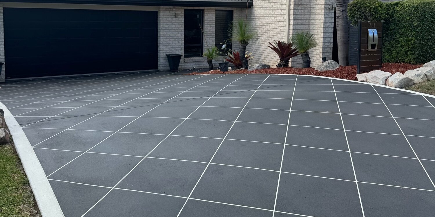 Driveway after covercrete resurfacing in Midnight Blue with a white stencilled tile pattern, running to a dark double garage door
