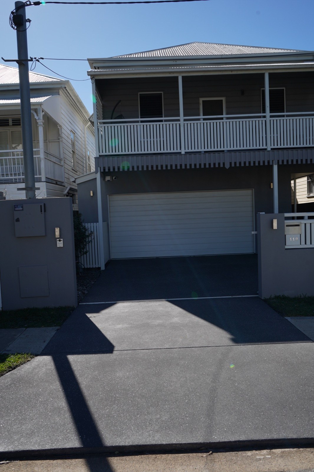 Freshly resurfaced dark charcoal driveway leading to the white garage of a two-storey Queenslander-style home