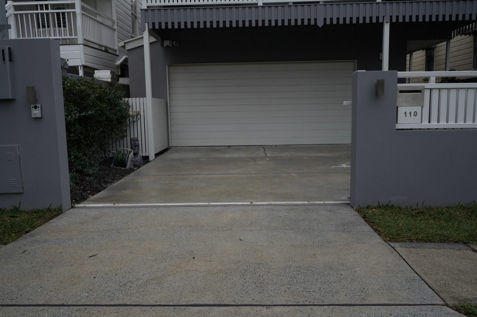 Worn pale grey concrete driveway with surface staining and an exposed-aggregate crossover, before spraycrete resurfacing